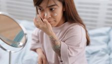 Seorang perempuan sedang mengaplikasikan pelembap pada wajahnya yang kering, menunjukkan pentingnya langkah hidrasi dalam rutinitas perawatan kulit. Pelembap yang tepat membantu mengunci kelembapan dan memperbaiki *skin barrier* kulit kering.