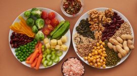 Piring yang berisi berbagai makanan bergizi seimbang, mencakup sayuran hijau segar, biji-bijian utuh, sumber protein seperti ikan, dan buah-buahan berwarna cerah, menunjukkan representasi visual dari pola makan sehat yang dianjurkan. Ilustrasi ini menekankan pentingnya variasi nutrisi dalam setiap sajian untuk mendukung kesehatan tubuh secara menyeluruh dan energi sepanjang hari.
