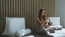 Seseorang sedang menikmati secangkir teh herbal sambil melihat pemandangan kota dari jendela, menunjukkan momen ketenangan dan mindfulness di tengah kesibukan perkotaan. Gambar ini merefleksikan pentingnya menciptakan ruang untuk relaksasi dalam gaya hidup sehat.