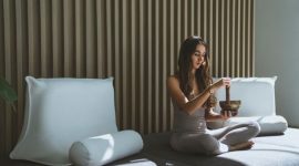 Seseorang sedang menikmati secangkir teh herbal sambil melihat pemandangan kota dari jendela, menunjukkan momen ketenangan dan mindfulness di tengah kesibukan perkotaan. Gambar ini merefleksikan pentingnya menciptakan ruang untuk relaksasi dalam gaya hidup sehat.