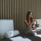 Seseorang sedang menikmati secangkir teh herbal sambil melihat pemandangan kota dari jendela, menunjukkan momen ketenangan dan mindfulness di tengah kesibukan perkotaan. Gambar ini merefleksikan pentingnya menciptakan ruang untuk relaksasi dalam gaya hidup sehat.