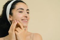 Seorang perempuan dengan kulit wajah bersih dan bercahaya alami memancarkan kepercayaan diri, menunjukkan bahwa perawatan kulit yang tepat menghasilkan kilau sehat dari dalam. Berbagai produk perawatan kulit yang sederhana dan efektif menemaninya, menyoroti pentingnya rutinitas yang konsisten.
