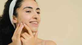 Seorang perempuan dengan kulit wajah bersih dan bercahaya alami memancarkan kepercayaan diri, menunjukkan bahwa perawatan kulit yang tepat menghasilkan kilau sehat dari dalam. Berbagai produk perawatan kulit yang sederhana dan efektif menemaninya, menyoroti pentingnya rutinitas yang konsisten.