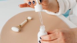 Seorang wanita sedang mengaplikasikan serum anti-aging di wajahnya, menunjukkan komitmen pada rutinitas perawatan kulit untuk menjaga keremajaan dan kesehatan kulit. Ilustrasi ini menggambarkan pentingnya perawatan teratur sebagai bagian dari upaya mendapatkan kulit awet muda.