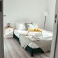 Sebuah kamar tidur minimalis dengan dominasi warna putih dan abu-abu muda, dilengkapi furnitur kayu sederhana dan pot tanaman hijau, menciptakan suasana yang menenangkan dan rapi. Desain interior ini menonjolkan prinsip 