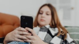 Seorang remaja yang tampak murung sedang menatap layar ponselnya, merefleksikan isolasi dan tekanan yang seringkali dialami generasi muda di tengah arus deras dunia digital. Gambar ini menggambarkan pentingnya perhatian dan dukungan terhadap kesehatan mental mereka di era modern ini.