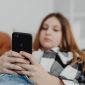 Seorang remaja yang tampak murung sedang menatap layar ponselnya, merefleksikan isolasi dan tekanan yang seringkali dialami generasi muda di tengah arus deras dunia digital. Gambar ini menggambarkan pentingnya perhatian dan dukungan terhadap kesehatan mental mereka di era modern ini.