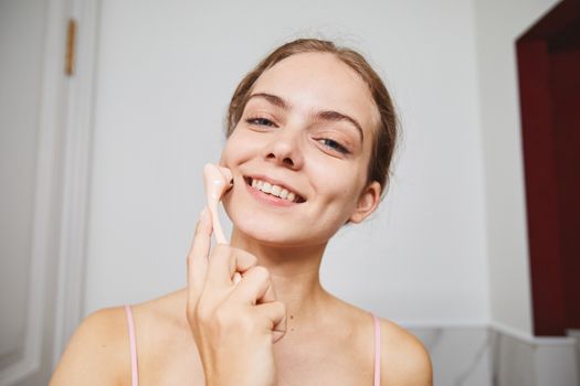 Seorang remaja perempuan sedang tersenyum sambil memegang produk perawatan kulit di kamar mandi, menunjukkan pentingnya rutinitas skincare yang tepat untuk kulit muda. Pemilihan produk yang lembut dan sesuai kebutuhan kulit remaja sangat penting untuk menjaga kesehatan dan kecerahan alami kulit mereka.