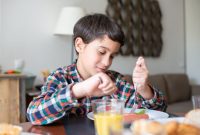 Seorang remaja tersenyum ceria sambil memegang piring berisi makanan sehat yang beragam, menunjukkan pentingnya keseimbangan nutrisi untuk mendukung pertumbuhan optimal dan energi sepanjang hari. Makanan sehat ini terdiri dari protein, sayuran, dan buah-buahan segar.