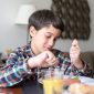 Seorang remaja tersenyum ceria sambil memegang piring berisi makanan sehat yang beragam, menunjukkan pentingnya keseimbangan nutrisi untuk mendukung pertumbuhan optimal dan energi sepanjang hari. Makanan sehat ini terdiri dari protein, sayuran, dan buah-buahan segar.