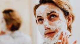 Seorang remaja perempuan sedang mengaplikasikan pembersih wajah yang lembut pada kulitnya, menunjukkan langkah awal dalam rutinitas perawatan kulit yang aman dan tepat. Produk yang tepat akan membantu menjaga kesehatan kulit muda tanpa memicu iritasi.
