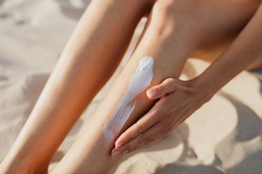 Seorang wanita sedang mengaplikasikan tabir surya di wajahnya saat berada di pantai, menunjukkan pentingnya perlindungan kulit dari sengatan matahari. Penggunaan tabir surya yang benar adalah kunci untuk menjaga kesehatan dan kecantikan kulit di bawah teriknya sinar UV.