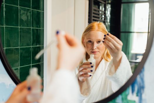 Seorang wanita tersenyum sambil mengaplikasikan serum wajah di pagi hari, menggambarkan rutinitas perawatan kulit yang konsisten untuk mendapatkan kulit sehat dan bercahaya. Rutinitas perawatan wajah yang teratur merupakan investasi jangka panjang untuk kesehatan kulit optimal.