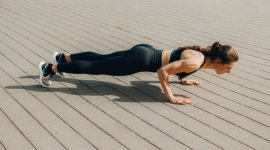 Seorang wanita sedang melakukan latihan angkat beban dengan *dumbbell* di sebuah pusat kebugaran, menunjukkan fokus pada pembentukan otot tangan dan bahu. Latihan resistensi merupakan kunci utama untuk membangun massa otot yang kuat dan kencang.