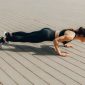 Seorang wanita sedang melakukan latihan angkat beban dengan *dumbbell* di sebuah pusat kebugaran, menunjukkan fokus pada pembentukan otot tangan dan bahu. Latihan resistensi merupakan kunci utama untuk membangun massa otot yang kuat dan kencang.