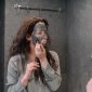 Seorang wanita tersenyum sembari mengaplikasikan masker wajah alami dari bahan-bahan dapur, menunjukkan kemudahan dan kesenangan dalam merawat kulit secara tradisional di rumah.