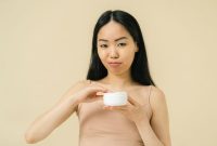 Seorang wanita sedang mengaplikasikan pelembap pada wajahnya, menunjukkan kesederhanaan dan ketelatenan dalam rutinitas perawatan kulit sehari-hari yang efektif. Gambar ini merepresentasikan pendekatan minimalis untuk mendapatkan kulit sehat dan bercahaya.