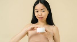Seorang wanita sedang mengaplikasikan pelembap pada wajahnya, menunjukkan kesederhanaan dan ketelatenan dalam rutinitas perawatan kulit sehari-hari yang efektif. Gambar ini merepresentasikan pendekatan minimalis untuk mendapatkan kulit sehat dan bercahaya.