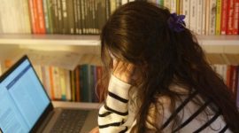 Seorang mahasiswa terlihat kewalahan dengan tumpukan buku dan tugas di depan laptopnya di kampus, menggambarkan tekanan akademik yang sering dialami selama masa perkuliahan. Ekspresi kelelahan dan cemas terlihat jelas pada wajahnya, merefleksikan pentingnya strategi pengelolaan stres.
