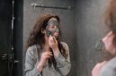 Seorang wanita sedang mengaplikasikan masker wajah buatan sendiri menggunakan bahan-bahan alami di dapur, menunjukkan kemudahan dan kepraktisan perawatan kecantikan dari rumah. Ia terlihat menikmati proses merawat kulit dengan sentuhan natural yang menyegarkan.