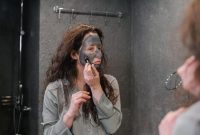 Seorang wanita sedang mengaplikasikan masker wajah buatan sendiri menggunakan bahan-bahan alami di dapur, menunjukkan kemudahan dan kepraktisan perawatan kecantikan dari rumah. Ia terlihat menikmati proses merawat kulit dengan sentuhan natural yang menyegarkan.