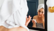 Seorang wanita sedang mengaplikasikan pelembap pada wajahnya yang kering, menunjukkan momen penting dalam rutinitas perawatan untuk mengembalikan hidrasi dan elastisitas kulit. Tindakan sederhana ini merupakan kunci untuk mendapatkan kulit wajah yang sehat dan terhindar dari sensasi tertarik akibat kering.