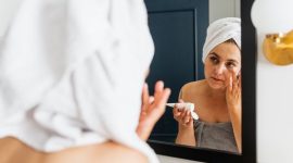 Seorang wanita sedang mengaplikasikan pelembap pada wajahnya yang kering, menunjukkan momen penting dalam rutinitas perawatan untuk mengembalikan hidrasi dan elastisitas kulit. Tindakan sederhana ini merupakan kunci untuk mendapatkan kulit wajah yang sehat dan terhindar dari sensasi tertarik akibat kering.