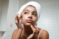 Seorang remaja perempuan dengan senyum cerah sedang mengaplikasikan pembersih wajah lembut, menunjukkan rutinitas perawatan kulit dasar yang aman untuk menjaga kesehatan kulit di usia muda. Pemilihan produk yang tepat merupakan kunci utama dalam merawat kulit remaja yang masih rentan terhadap perubahan hormon.