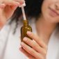 Seorang wanita mengaplikasikan serum wajah, menunjukkan salah satu langkah penting dalam rutinitas perawatan untuk mengatasi jerawat dan menjaga kesehatan kulit. Penggunaan serum yang tepat dapat membantu mengurangi peradangan serta produksi minyak berlebih pada wajah.