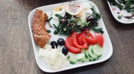 Sebuah piring berisi makanan seimbang dengan beragam warna menunjukkan kombinasi nasi merah, protein ikan panggang, dan sayuran segar, menggambarkan pilihan menu sehat yang menggugah selera.