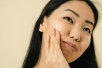 Seorang wanita sedang mengaplikasikan pelembap wajah, menunjukkan pentingnya hidrasi dalam rutinitas perawatan kulit sehari-hari untuk menjaga elastisitas dan cahaya alami kulit.