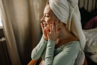 Seorang wanita tersenyum cerah menunjukkan kulit wajahnya yang glowing setelah mengaplikasikan produk perawatan kulit di pagi hari. Kilau sehat pada kulitnya memancarkan aura segar dan percaya diri.