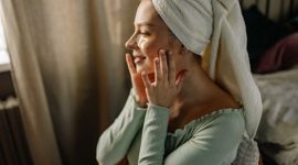 Seorang wanita tersenyum cerah menunjukkan kulit wajahnya yang glowing setelah mengaplikasikan produk perawatan kulit di pagi hari. Kilau sehat pada kulitnya memancarkan aura segar dan percaya diri.