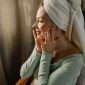 Seorang wanita tersenyum cerah menunjukkan kulit wajahnya yang glowing setelah mengaplikasikan produk perawatan kulit di pagi hari. Kilau sehat pada kulitnya memancarkan aura segar dan percaya diri.