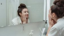 Seorang wanita sedang memeriksa kondisi wajahnya di cermin, merefleksikan perjalanan panjang dalam mengatasi jerawat dan upaya meraih kulit yang lebih sehat. Gambar ini secara visual menangkap momen introspeksi dan harapan untuk kulit yang bersih.
