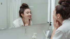 Seorang wanita sedang memeriksa kondisi wajahnya di cermin, merefleksikan perjalanan panjang dalam mengatasi jerawat dan upaya meraih kulit yang lebih sehat. Gambar ini secara visual menangkap momen introspeksi dan harapan untuk kulit yang bersih.