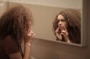 Remaja perempuan sedang membersihkan wajah di depan cermin kamar mandi, menunjukkan pentingnya rutinitas perawatan kulit dasar yang konsisten. Memilih produk yang tepat adalah kunci untuk menjaga kulit tetap sehat selama masa pubertas.