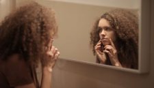 Remaja perempuan sedang membersihkan wajah di depan cermin kamar mandi, menunjukkan pentingnya rutinitas perawatan kulit dasar yang konsisten. Memilih produk yang tepat adalah kunci untuk menjaga kulit tetap sehat selama masa pubertas.