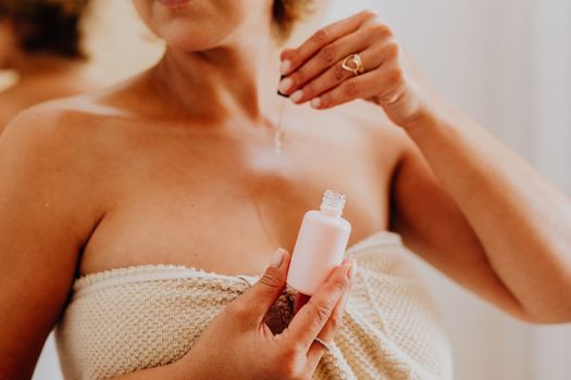 Seorang wanita mengaplikasikan serum vitamin C pada wajahnya, menunjukkan langkah penting dalam rutinitas perawatan kulit untuk mendapatkan kulit yang lebih cerah dan sehat. Penggunaan serum secara teratur dapat membantu menutrisi kulit secara mendalam dan melindunginya dari berbagai faktor lingkungan yang merusak.